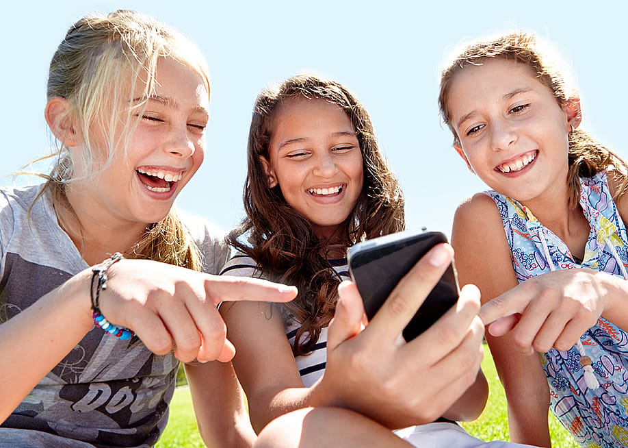 A group of three young girls laughing at content on social media. — PeopleImages // Shutterstock