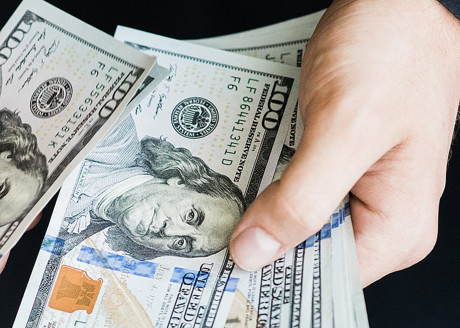 A person's hand counting $100 dollar bills. — Tayler Derden // Shutterstock