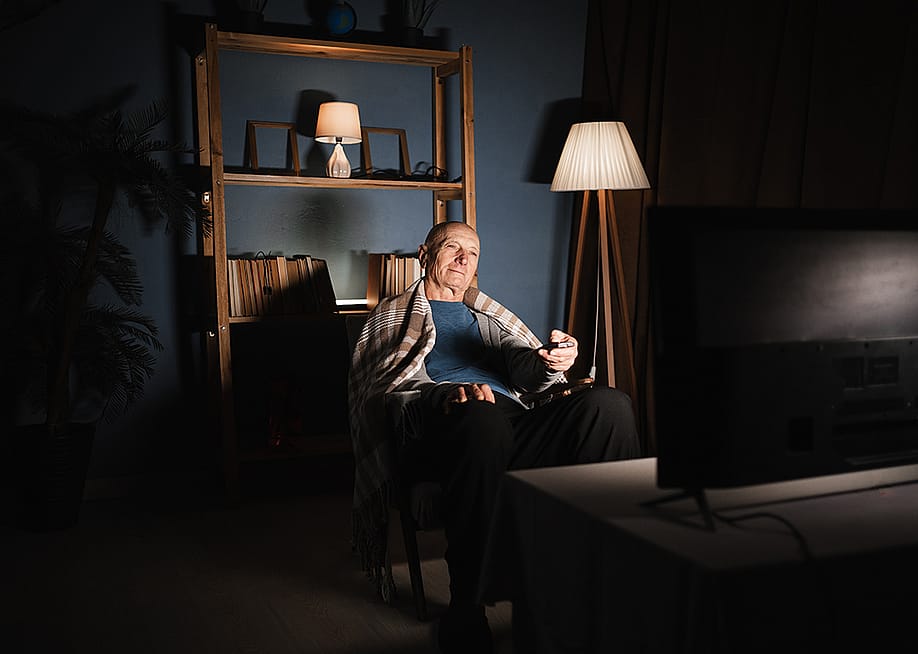 An elderly man sitting in a dim living room and watching TV. — Lysenko Andrii // Shutterstock