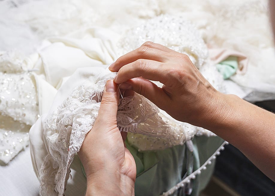 Hands of a seamstress sewing beads on a wedding dress. — nazileozturk // Shutterstock