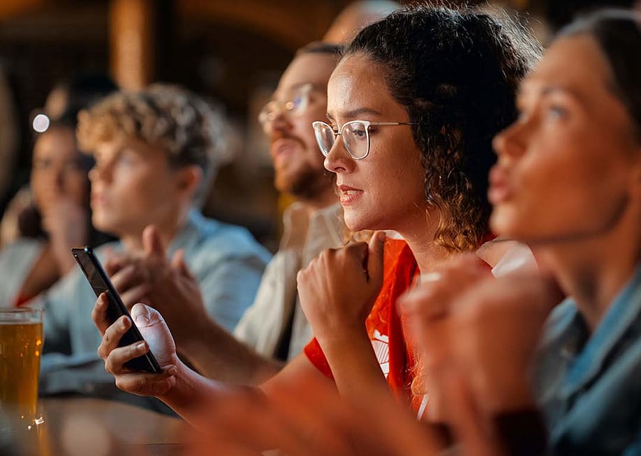 A female football fan in a bar monitoring game results on her phone. — Gorodenkoff // Shutterstock