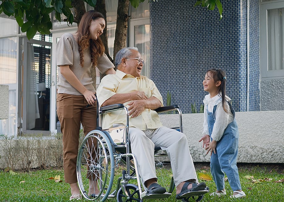 A disabled senior grandfather with his daughter and grandchild in a park. — Sorapop Udomsri // Shutterstock