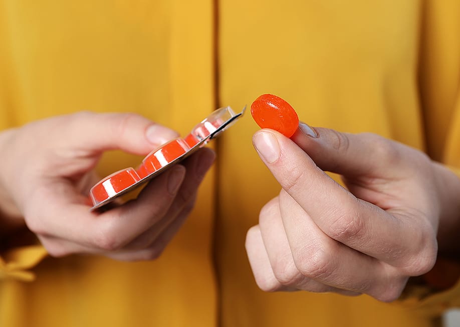 A woman holding a red cough drop tablet. — New Africa // Shutterstock