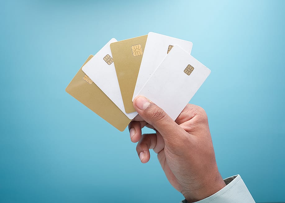 A hand holding an assortment of five gold and white credit card against a blue background. — Towfiqu ahamed barbhuiya // Shutterstock