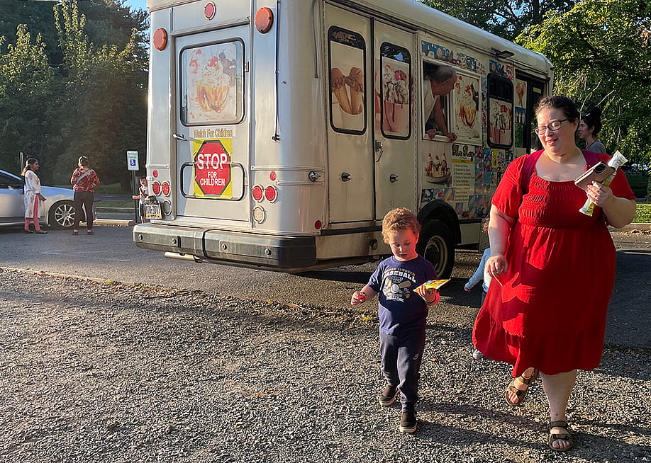 Kimberly Halevy wearing a crimson red midi dress with mid-length sleeves walks with her son Joshua beside her, enjoy treats from an ice cream truck visible behind them, after a recent session with a special instructor. — Rebecca Redelmeier // Chalkbeat