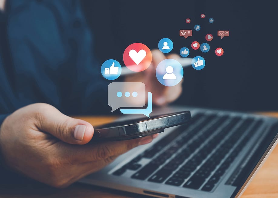 Social media interaction graphics illustrated over a person using a smartphone and laptop. — Anucha Tiemsom // Shutterstock
