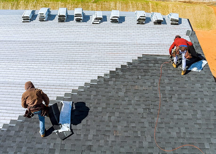 Aerial view of roof workers installing shingles using hammer and nail. — ungvar // Shutterstock