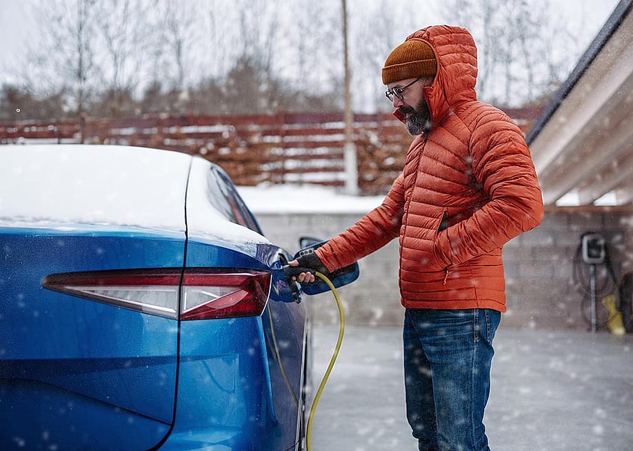A man charging his EV during a snowy day. — Halfpoint // Shutterstock