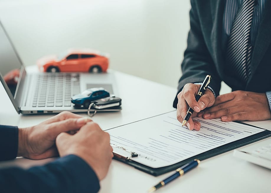 Figures of cars surround a table while a car salesperson transacts with a customer. — SaiArLawKa2 // Shutterstock