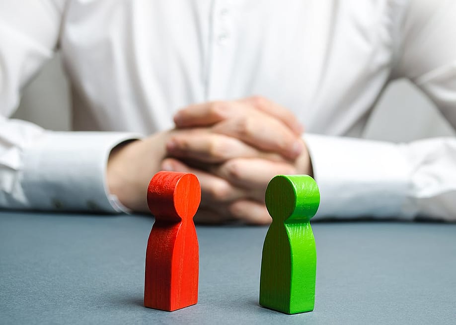 An arbitrator visualizing conflict situation between people depicted by two wooden figures. — Andrii Yalanskyi // Shutterstock