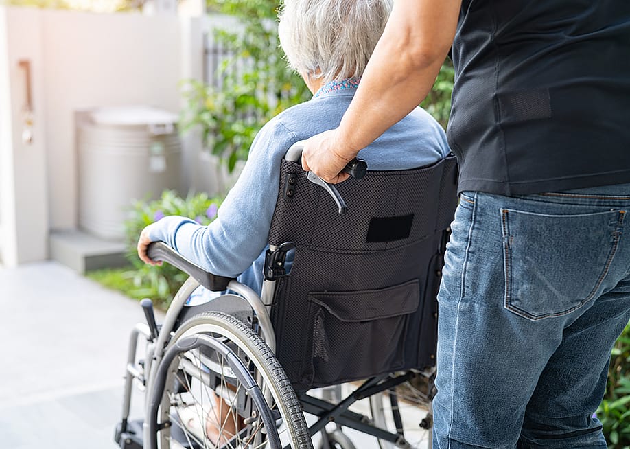 A caregiver caring for an elderly woman in a wheelchair. — sasirin pamai // Shutterstock