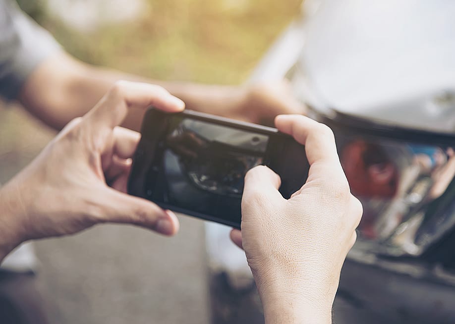 An insurance agent taking a photo of a car's damage. — Pair Srinrat // Shutterstock