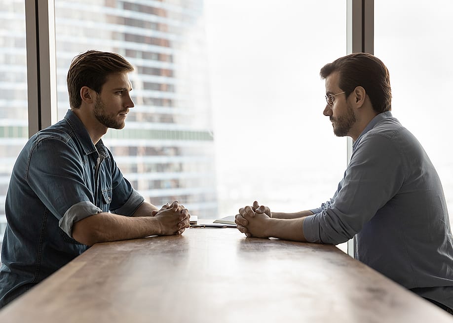 Two businessmen sitting across a table from each other engaged in discussion. — fizkes // Shutterstock