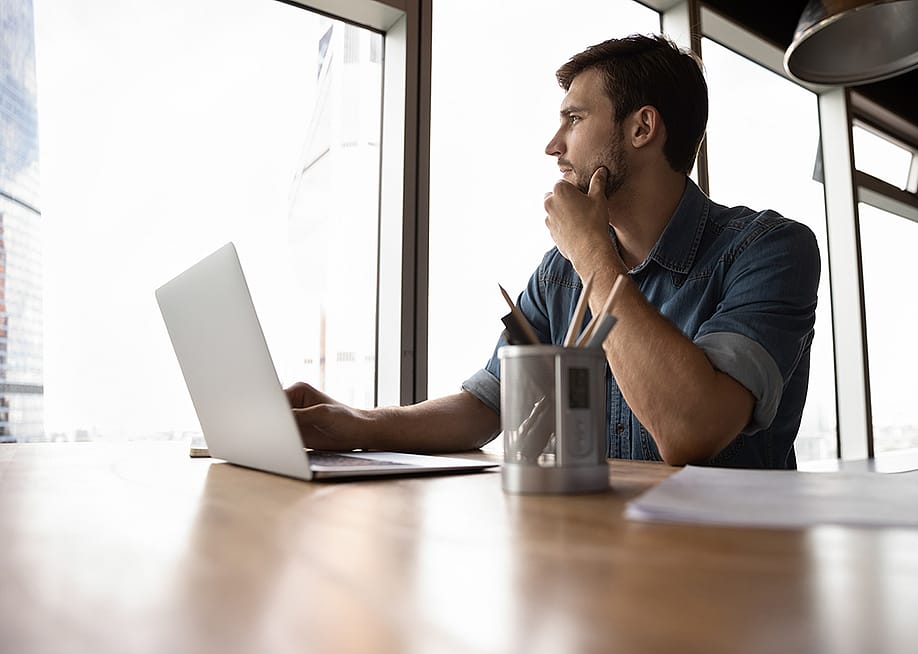 A male professional looking out the office window, pondering on work decisions. — fizkes // Shutterstock