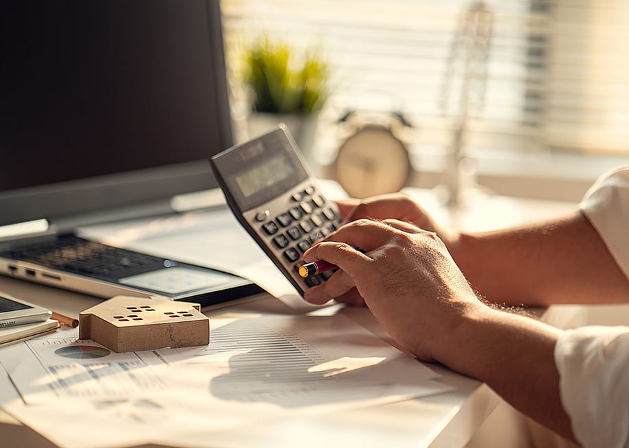A real estate professional using a calculator over tax documents. — godshutter // Shutterstock