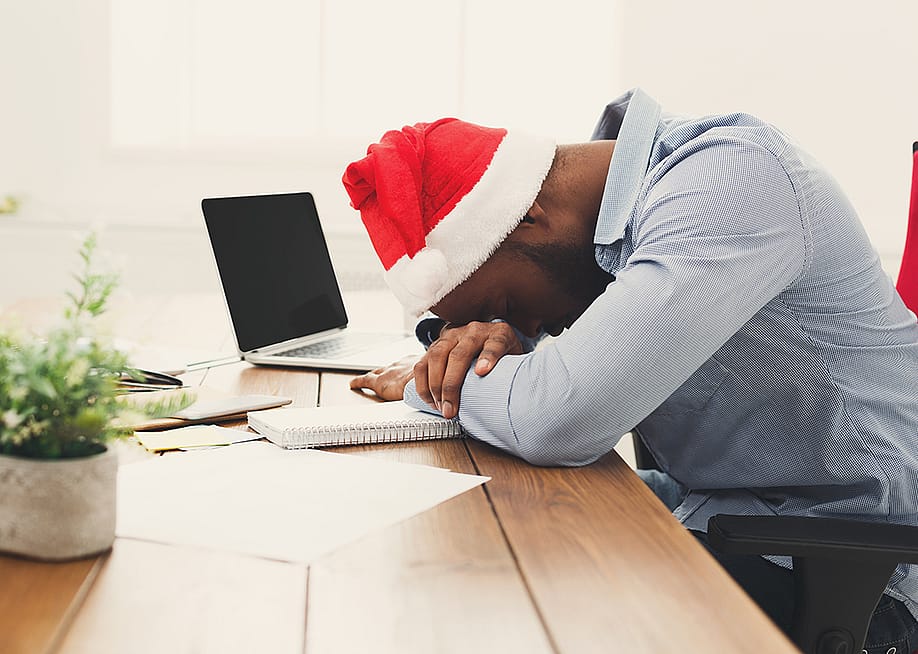 A tired businessman wearing a Christmas hat while asleep at work. — Prostock-studio // Shutterstock