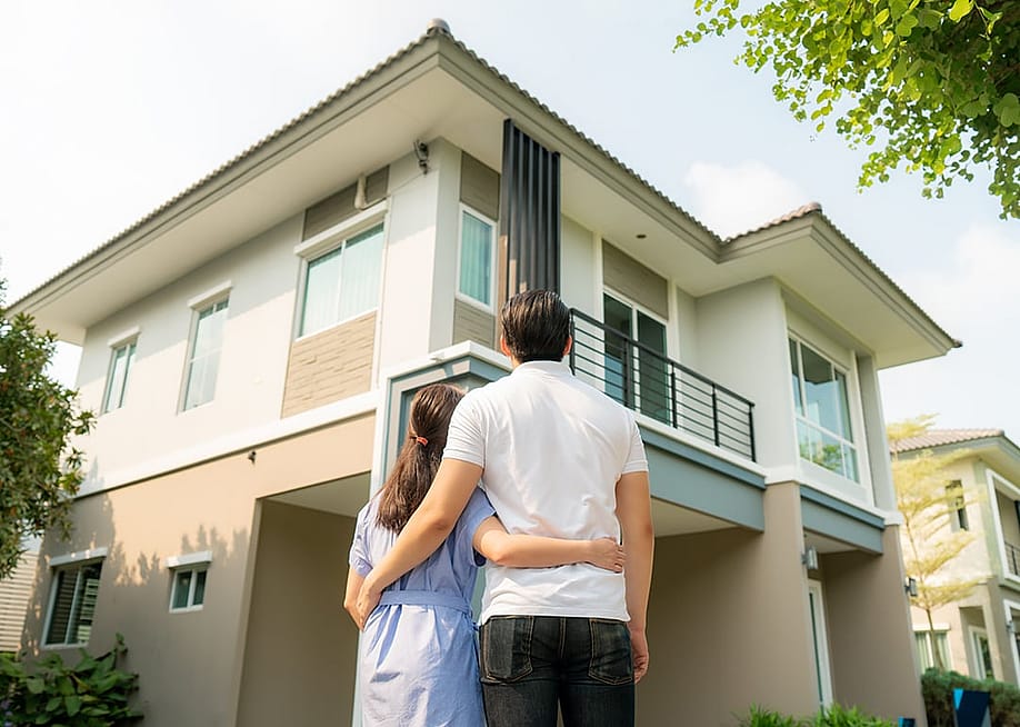 Back portrait of a young couple standing in front of their newly-bought home. — PrasitRodphan // Shutterstock