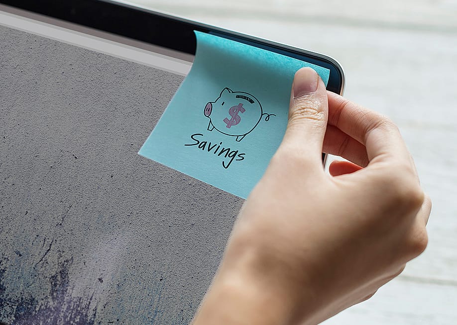 A person sticking a savings note on a computer screen. — Rawpixel.com // Shutterstock
