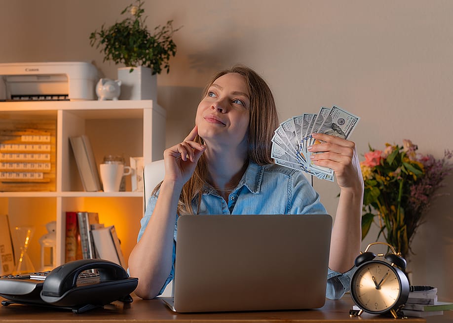 A female manager holding cash daydreaming in an office. — Anton27 // Shutterstock