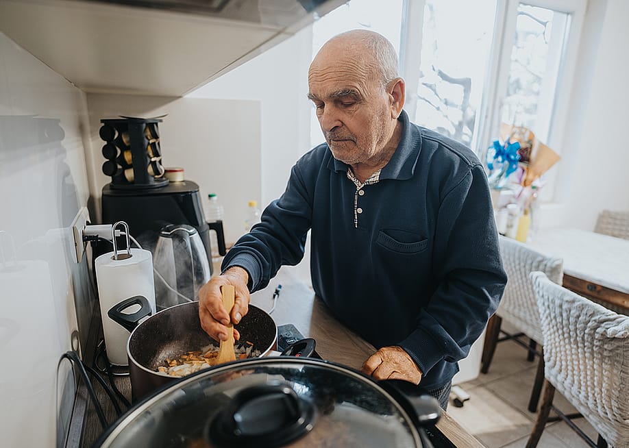 A senior man cooking a dish in his brightly-lit kitchen at home. — Gorgev // Shutterstock