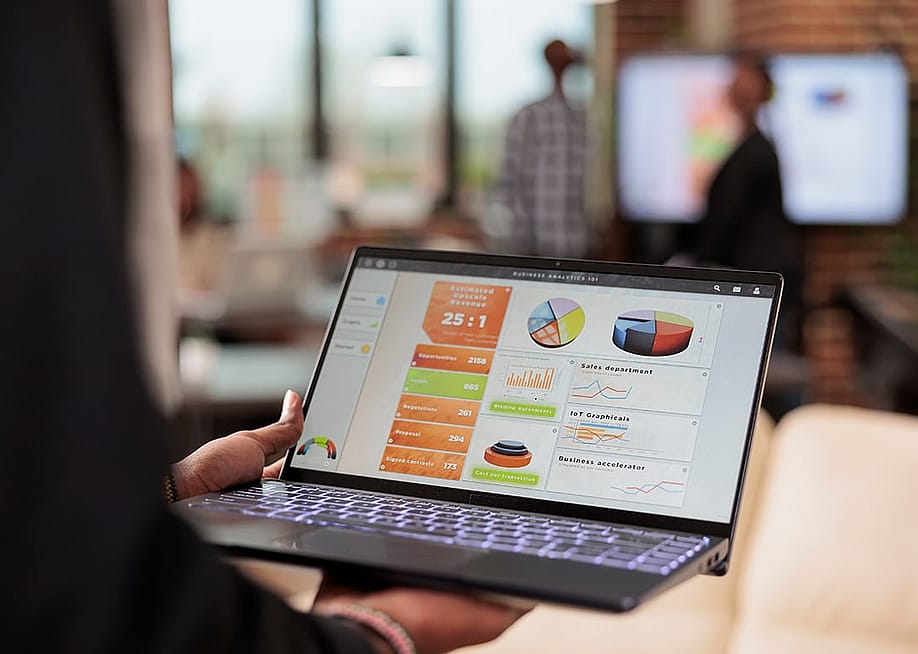 A businessperson holding a laptop that displays data charts and graphs. — DC Studio // Shutterstock