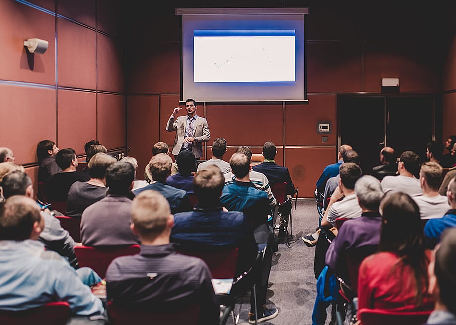 An audience in a conference room listening to a speaker. — Matej Kastelic // Shutterstock
