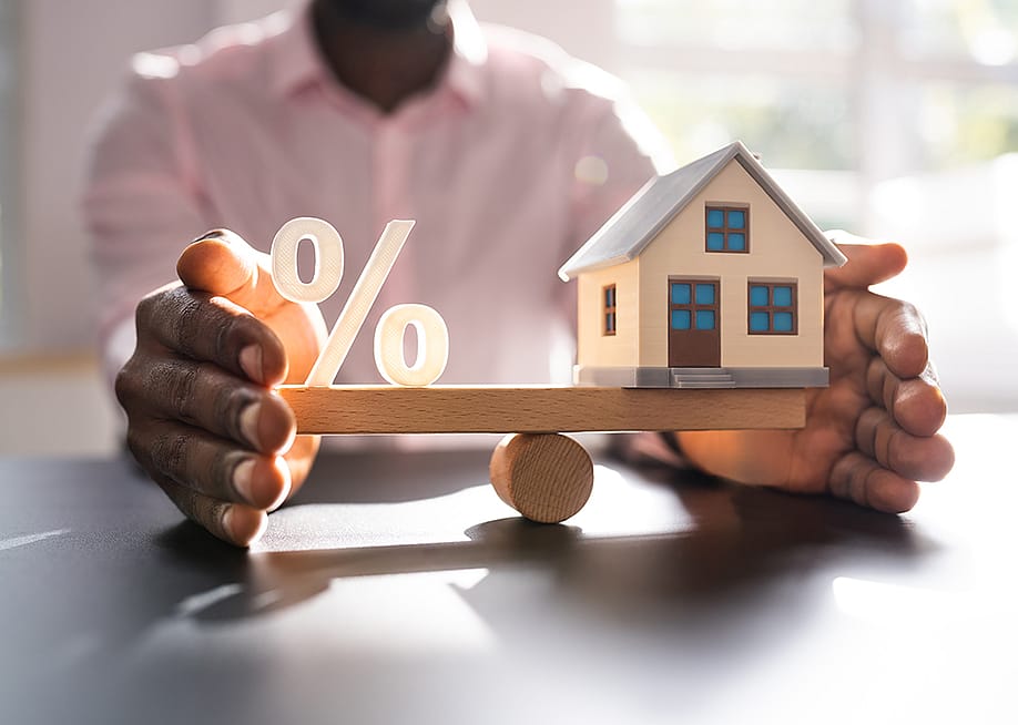 A person balancing figures of a percentage and a small house. — Andrey_Popov // Shutterstock