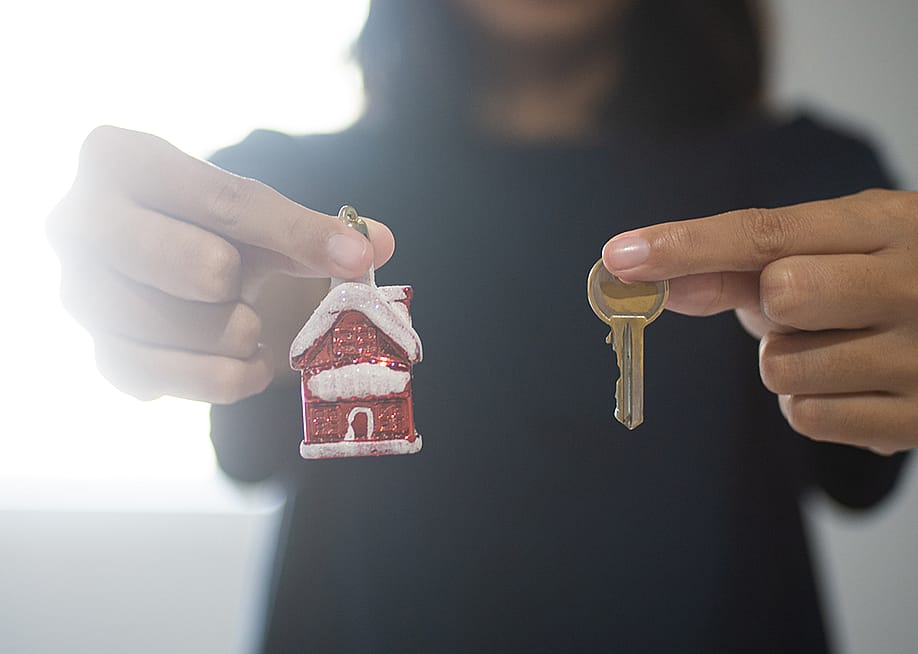 A woman holding a small figure of a Christmas home with her right hand and a house key with her left. — Yehez.Picture // Shutterstock