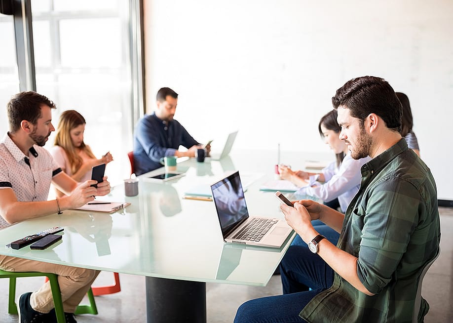 A business team in a meeting room but each member is using their phone. — antoniodiaz // Shutterstock