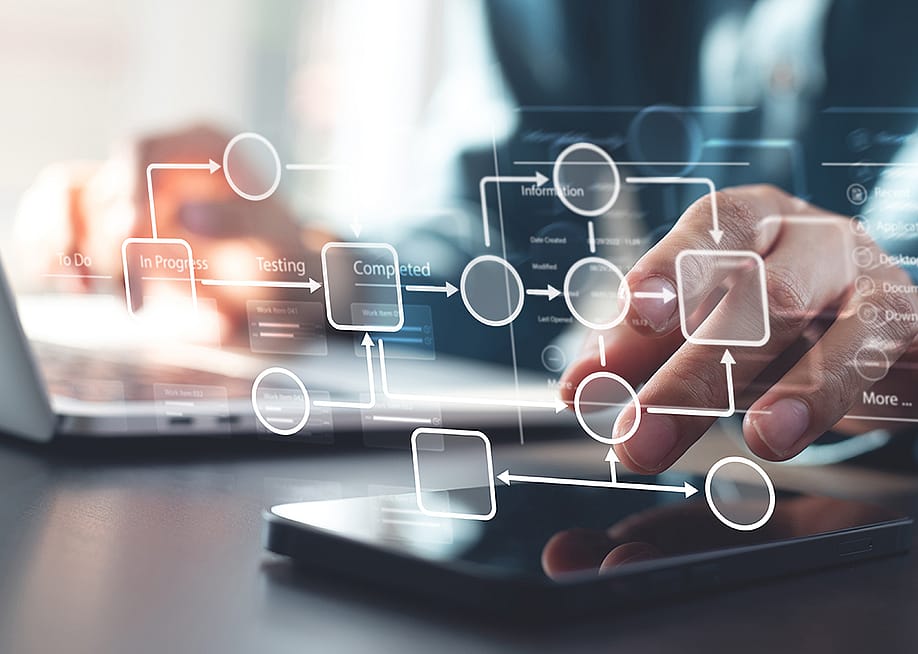 Person using a laptop and phone illustrated with automated business workflow chart graphics. — TippaPatt // Shutterstock
