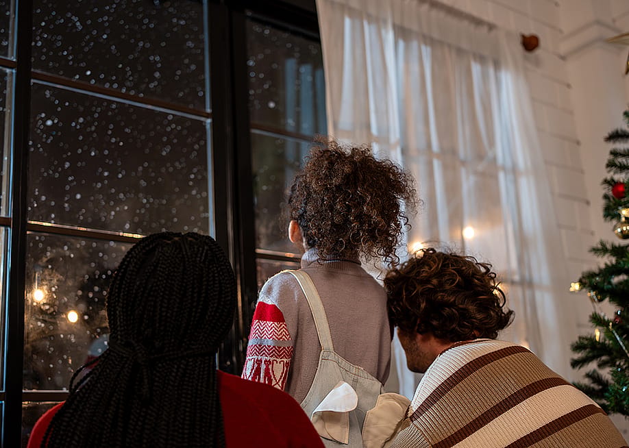 A family looking at the window to see snowfall at night. — Hananeko_Studio // Shutterstock