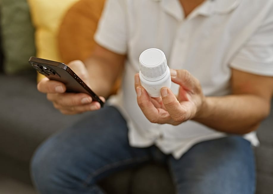 Person holding a prescription medicine bottle and checking info using smartphone. — Krakenimages.com // Shutterstock