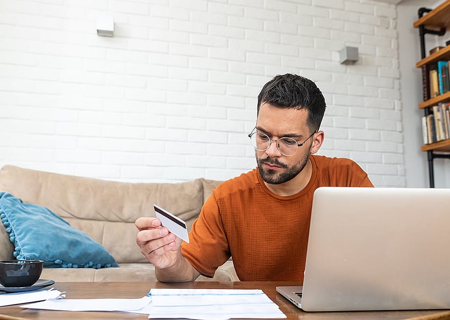 A stressed man reviewing credit card and utility expense documents at home. — Srdjan Randjelovic // Shutterstock