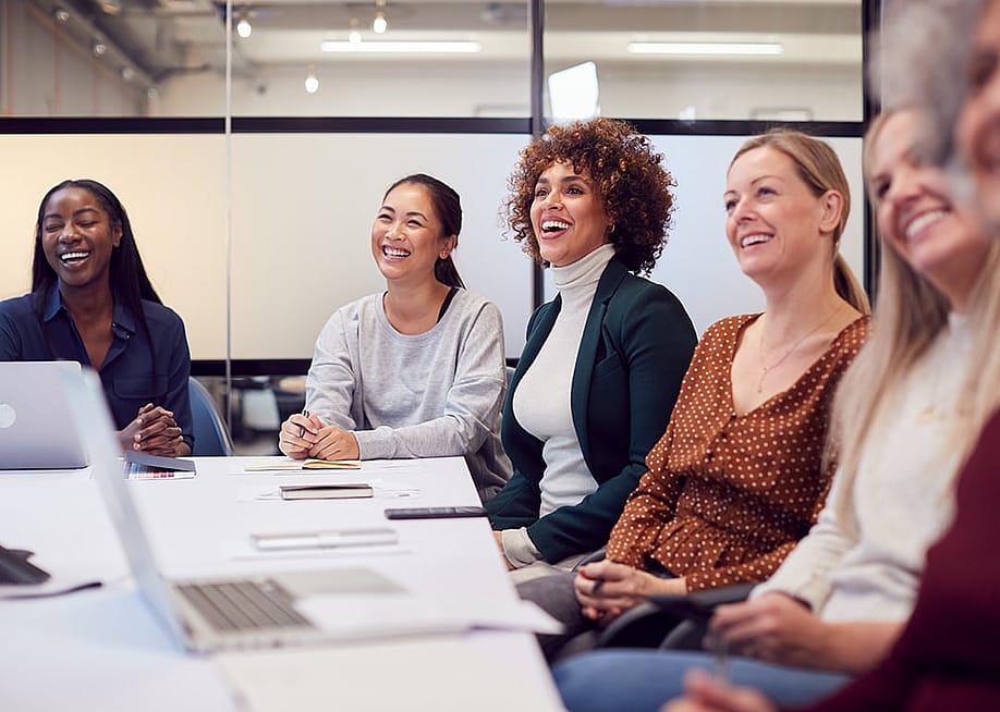 A group of business women listening to a presentation in a meeting room. — Monkey Business Images // Shutterstock