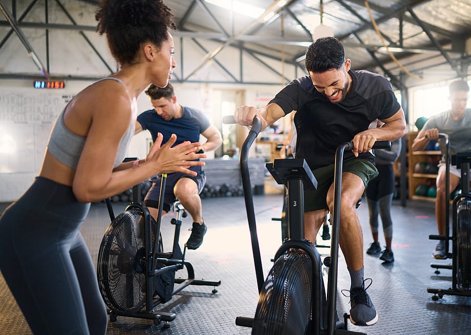 A trainer cheers on attendees of her spin class in a gym. — PeopleImages // Shutterstock