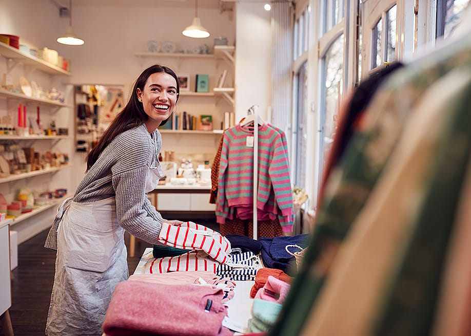 A female business owner arranging stock clothing for her store's window display. — Monkey Business Images // Shutterstock