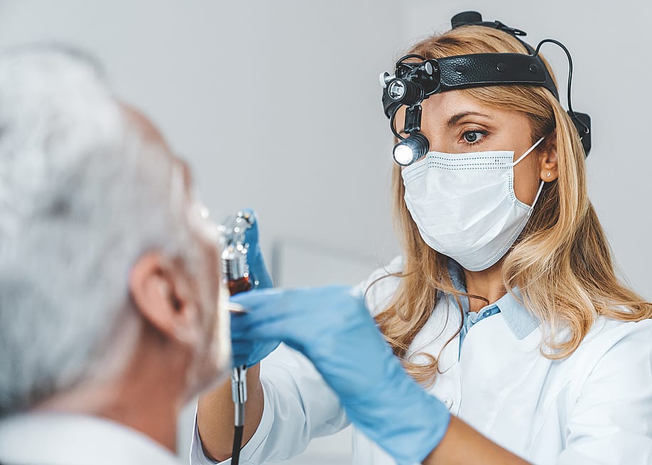 Close up of a female otolaryngologist making an examination of a senior patient's oral cavity. — Inside Creative House // Shutterstock