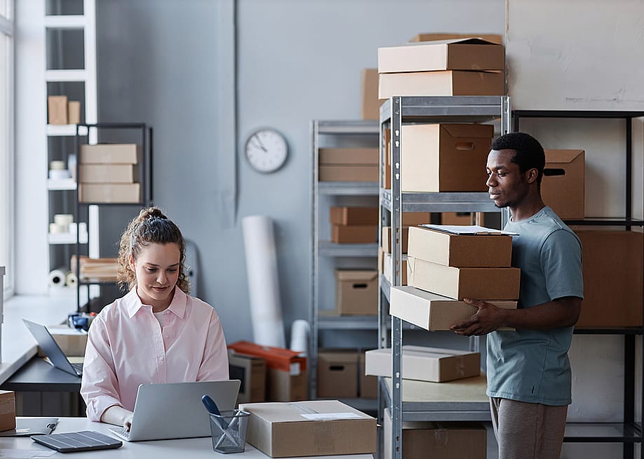 Two members of a small business in a warehouse preparing to send packages. — SeventyFour // Shutterstock