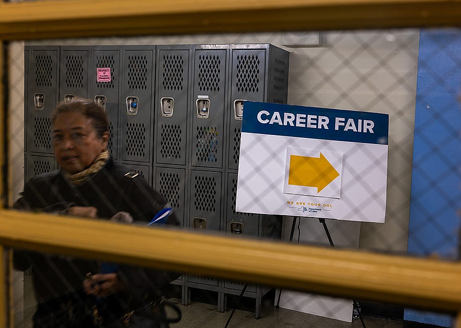 A window view of a jobseeker and a signage with an arrow pointing to where a career fair is situated in New York City. — Spencer Platt // Getty Images
