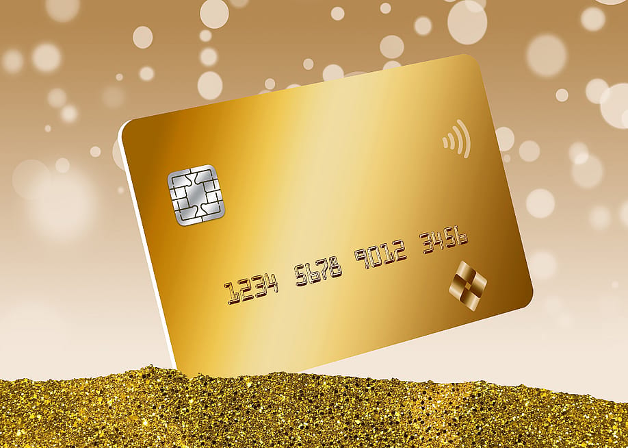 A gold credit card is seen in a pile of gold dust with bokeh circles in the background in a 3D illustration. — robertindiana // Shutterstock