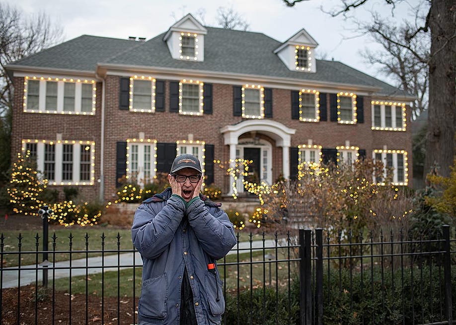 Person poses with the classic "Home Alone" pose with hands pressed to cheeks outside the gate of the home used in the film "Home Alone," in Winnetka, IL — Michael Gordon // Shutterstock