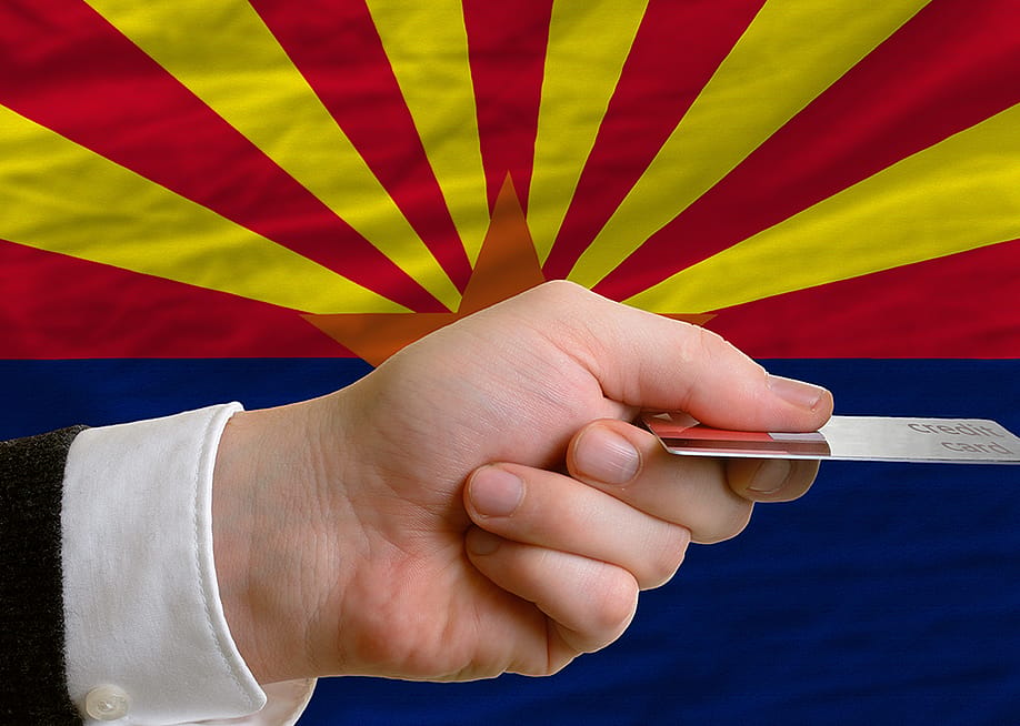 A person's hand holding a credit card with a background of Arizona's flag. — vepar5 // Shutterstock