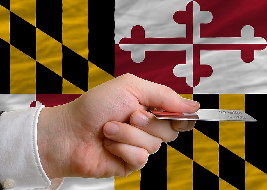 Person's hand holding a credit card with a background of Maryland's flag. — vepar5 // Shutterstock