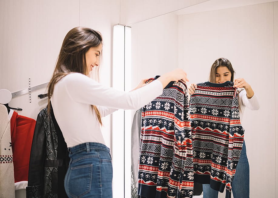 A young woman looking at a winter sweater in a dressing room. — Synergic Works OU // Shutterstock