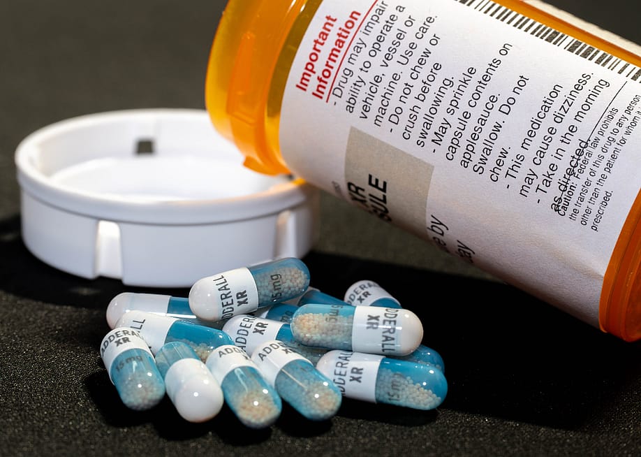 Closeup of an open bottle of adderral medication with some pills laying next to the bottle. — Alex Di Stasi // Shutterstock