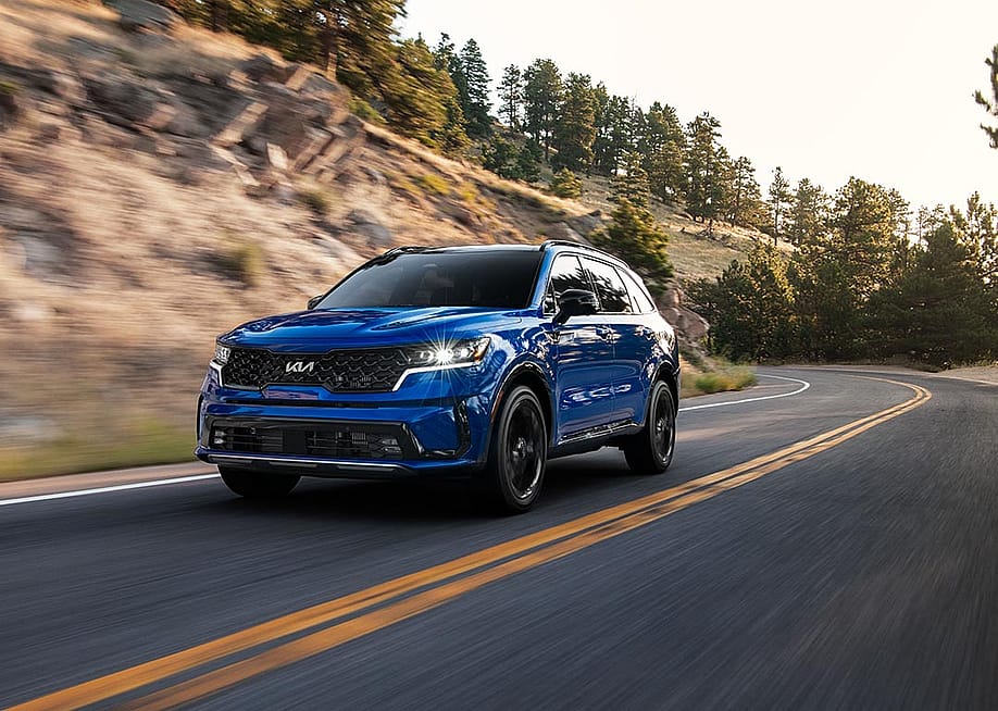 A front 3/4 view of a blue 2023 Sorento SX driving on a mountain road. — Robin Trajano // Kia America