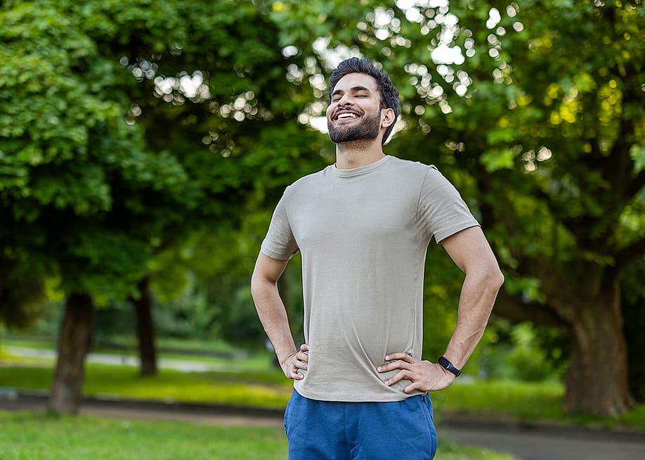 A sporty young man standing outdoors with hands on hips, smiling after an exercise. — TetianaKtv // Shutterstock