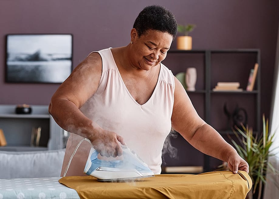 A senior woman happily ironing clothes at home. — SeventyFour // Shutterstock