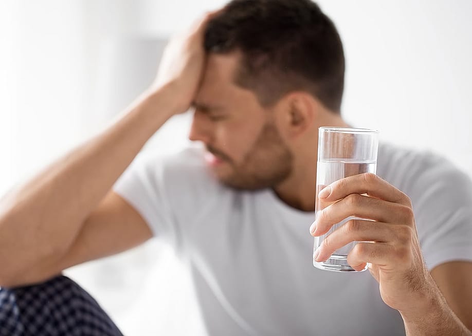 Man experiencing hangover holding a glass of water. — Ground Picture // Shutterstock