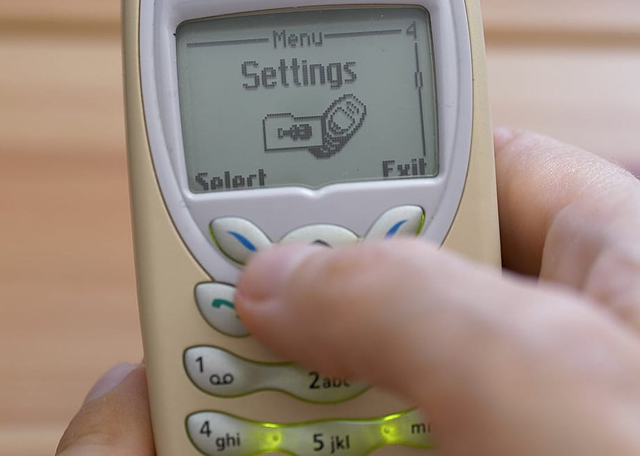 A retro Nokia 3410 mobile phone in someone's hand with the settings menu open. — zelvan // Shutterstock